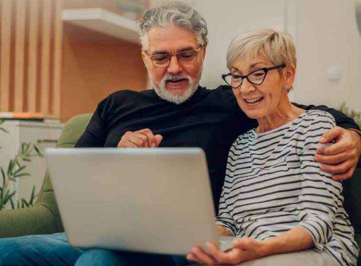 Retired couple smiling looking at something on a laptop
