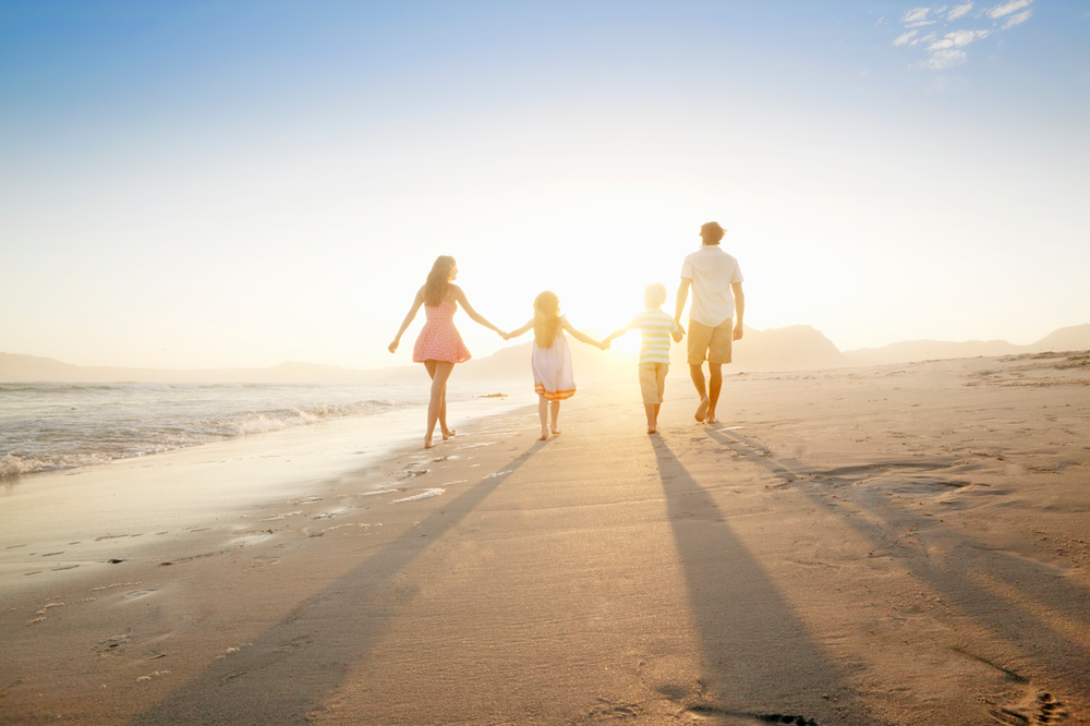 Young parents with children walking down a beach.
